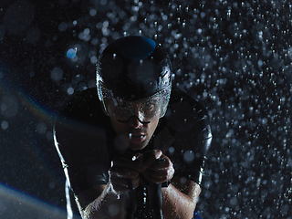 Image showing triathlon athlete riding bike on rainy night