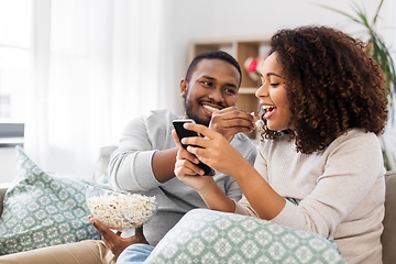 Image showing african couple with popcorn and smartphone at home