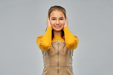 Image showing smiling teenage girl closing ears by hands