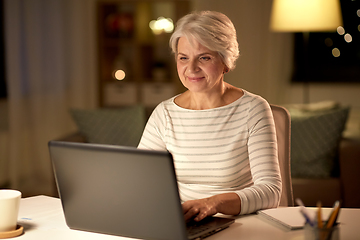 Image showing happy senior woman with laptop at home in evening