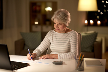 Image showing senior woman filling tax form at home in evening