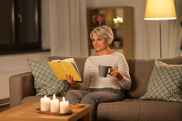 Image showing senior woman reading book and drinking tea at home