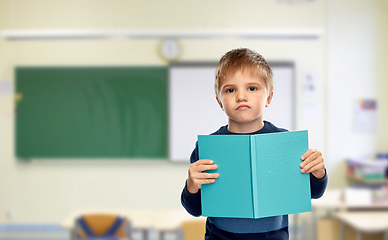 Image showing displeased little boy with book at school