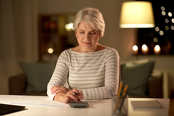 Image showing old woman counting on calculator at home at night