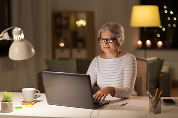 Image showing senior woman with laptop working at home at night