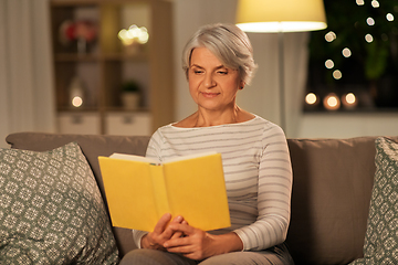 Image showing happy senior woman reading book at home in evening