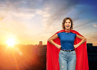 Image showing happy woman in red superhero cape over city sunset