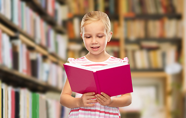 Image showing smiling little girl reading book at library