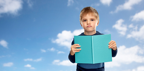 Image showing displeased little boy with book over blue sky