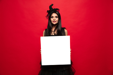 Image showing Young woman in hat and dress as a witch on red background