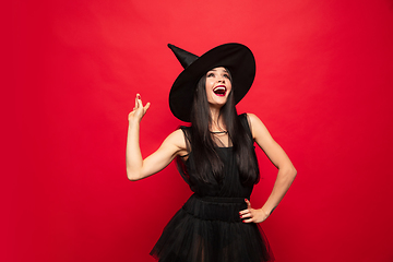 Image showing Young woman in hat and dress as a witch on red background