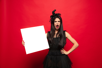 Image showing Young woman in hat and dress as a witch on red background