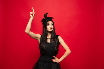 Image showing Young woman in hat and dress as a witch on red background