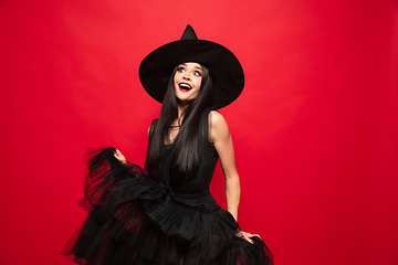 Image showing Young woman in hat and dress as a witch on red background