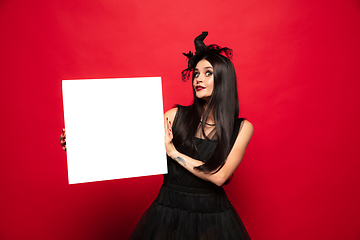 Image showing Young woman in hat and dress as a witch on red background