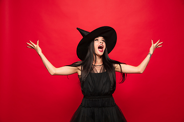 Image showing Young woman in hat and dress as a witch on red background