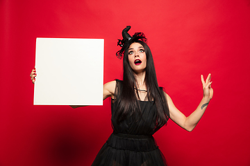 Image showing Young woman in hat and dress as a witch on red background