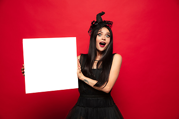 Image showing Young woman in hat and dress as a witch on red background