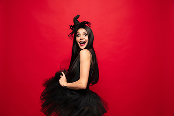 Image showing Young woman in hat and dress as a witch on red background