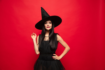 Image showing Young woman in hat and dress as a witch on red background