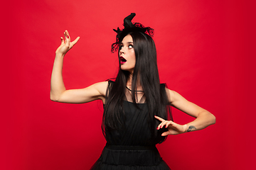 Image showing Young woman in hat and dress as a witch on red background