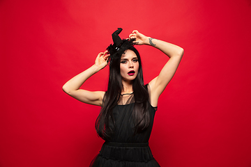 Image showing Young woman in hat and dress as a witch on red background