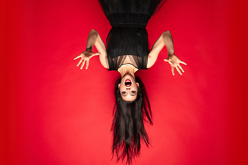 Image showing Young woman in hat and dress as a witch on red background