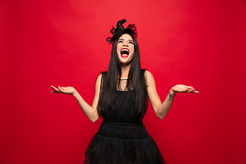 Image showing Young woman in hat and dress as a witch on red background