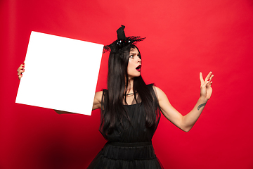 Image showing Young woman in hat and dress as a witch on red background