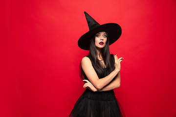 Image showing Young woman in hat and dress as a witch on red background