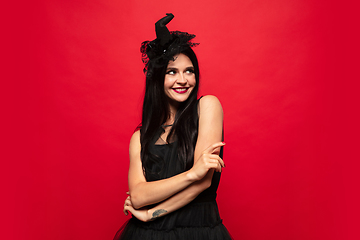 Image showing Young woman in hat and dress as a witch on red background