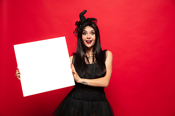 Image showing Young woman in hat and dress as a witch on red background