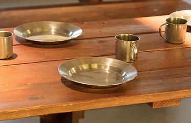 Image showing Very old metal cups and plates on a wooden table