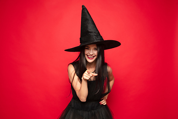 Image showing Young woman in hat and dress as a witch on red background