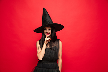 Image showing Young woman in hat and dress as a witch on red background