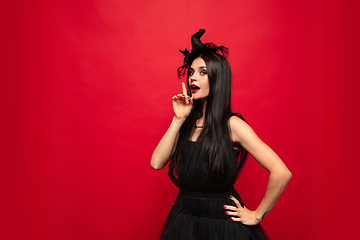 Image showing Young woman in hat and dress as a witch on red background