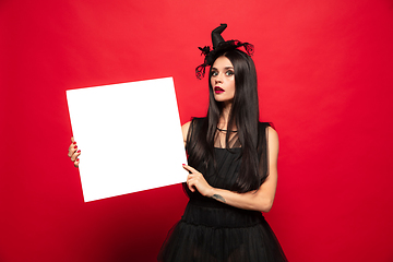 Image showing Young woman in hat and dress as a witch on red background