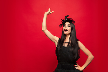 Image showing Young woman in hat and dress as a witch on red background