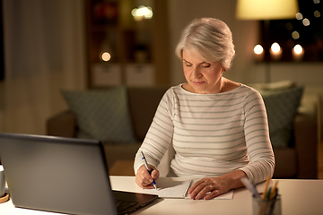 Image showing senior woman writing to notebook at home at night