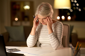 Image showing senior woman filling tax form at home in evening