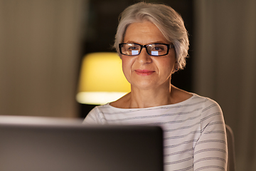 Image showing happy senior woman with laptop at home in evening