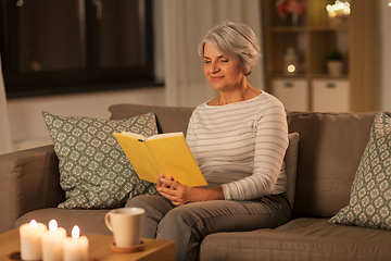 Image showing happy senior woman reading book at home in evening