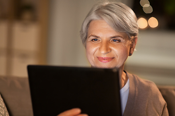 Image showing happy senior woman with tablet pc at home at night