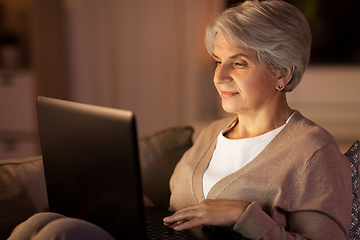 Image showing happy senior woman with laptop at home at night