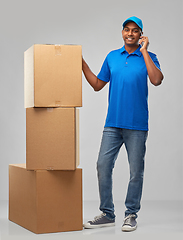 Image showing indian delivery man with boxes calls on smartphone