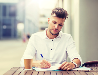 Image showing man with coffee and folder writing at city cafe