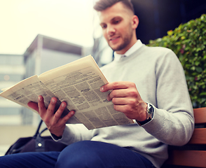 Image showing man reading newspaper on city street bench