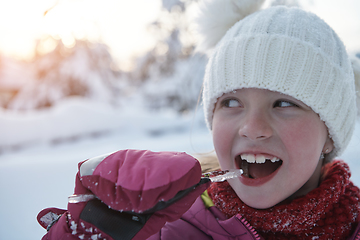 Image showing cute little girl while eating icicle on beautiful winter day