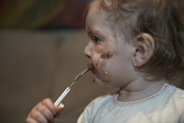 Image showing baby girl eating her chocolate desert with a spoon and making a mess