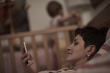 Image showing mother is using smarphone in bed while baby sleeping